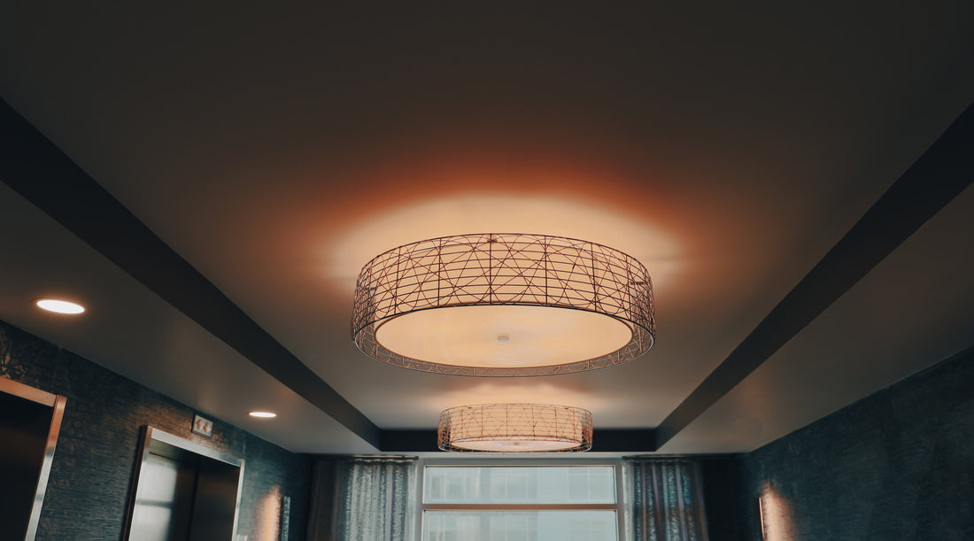 Glowing and lit drum flush mount light with black metal accents shown on a warm ceiling