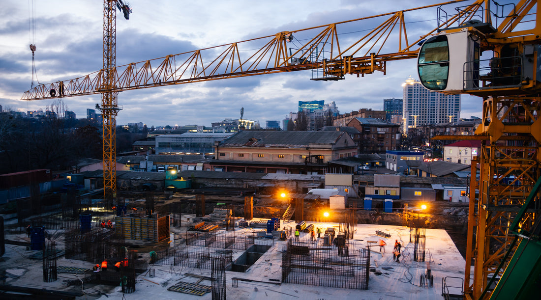 Temporary lighting illuminating construction site with cranes in the early evening