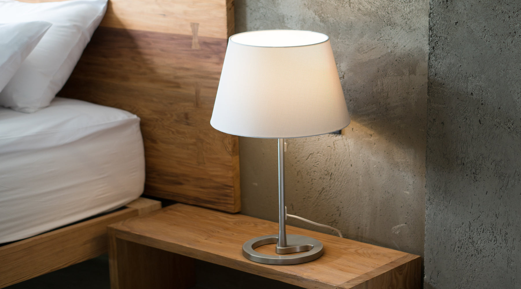 Modern table lamp on bedroom nightstand with bulb illuminated