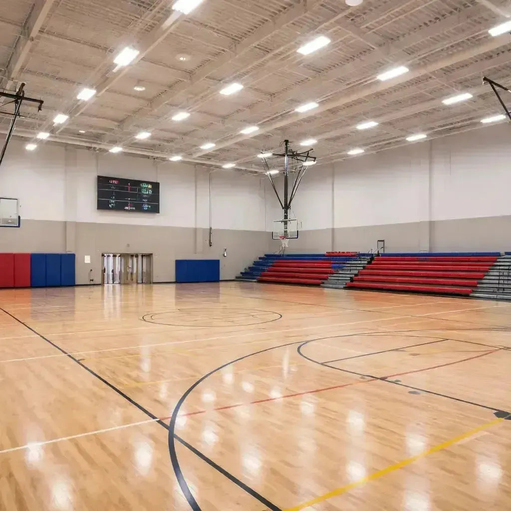 Linear LED light fixtures illuminating a commercial gymnasium with high ceilings, hardwood courts, and uniform overhead lighting