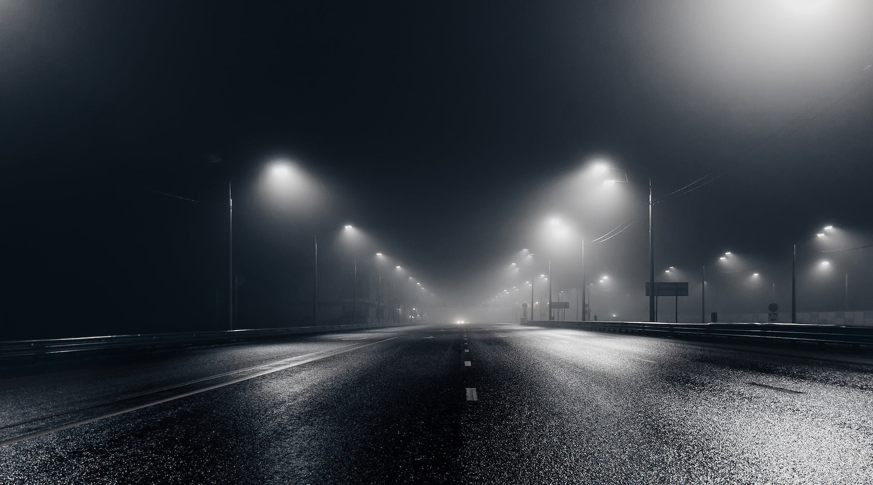 Street lighting shown illuminating foggy and misty roadway at night