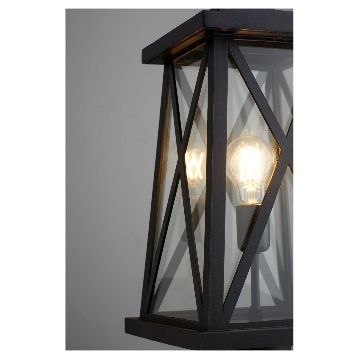 Black Outdoor Post Light with X-brace design, emitting warm glow. Enhance any outdoor space with timeless elegance. Brand: Quorum International.