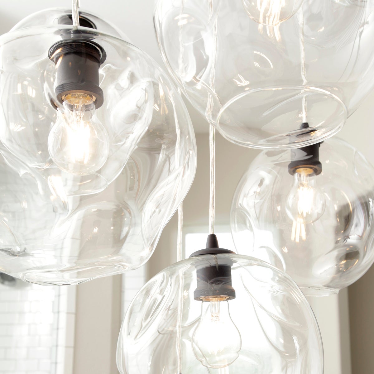 Cluster Pendant Light with clear glass lights and a close-up of a light bulb in a stylish metal fixture. Adjustable cord suspends the pendant lighting from a matching canopy. Perfect for brightening your space in contemporary style.