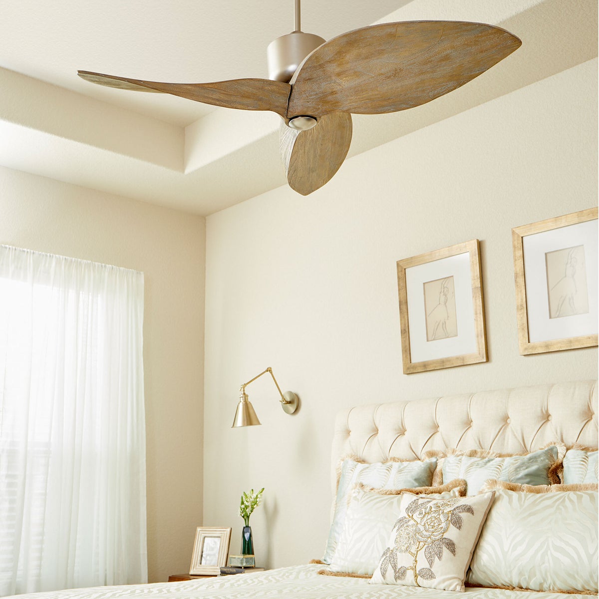 Contemporary Ceiling Fan in a bedroom with wooden blades, a white curtain, framed pictures, and a gold lamp on the wall.