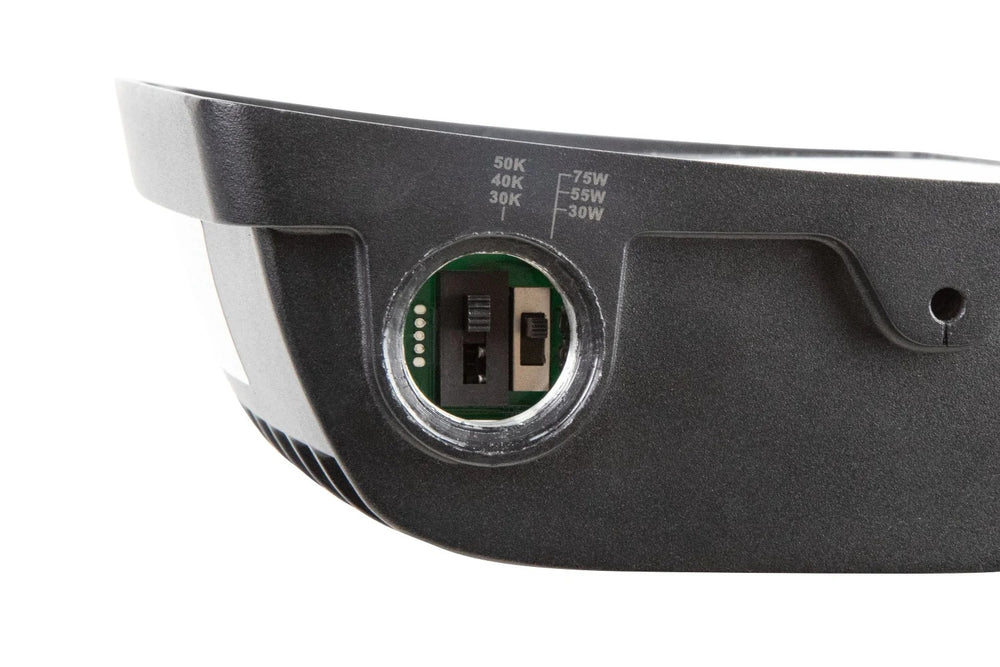 LED flood light side view with adjustable knuckle mount and housing knockout showing wattage-select and CCT-select slide (or DIP) switches; 120–277V input with 0–10V dimming, IP65 rated, 5/10/15W selectable configurations producing 650–1,950 lumens with 3000K/4000K/5000K options.