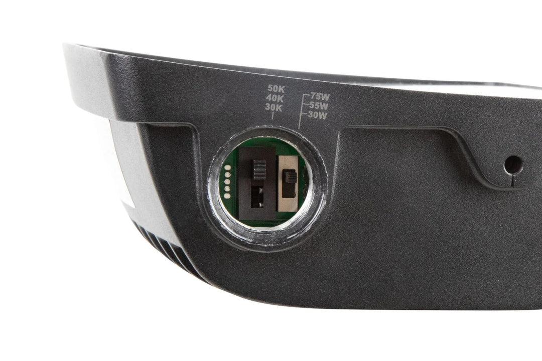 LED flood light side view with adjustable knuckle mount and housing knockout showing wattage-select and CCT-select slide (or DIP) switches; 120–277V input with 0–10V dimming, IP65 rated, 5/10/15W selectable configurations producing 650–1,950 lumens with 3000K/4000K/5000K options.