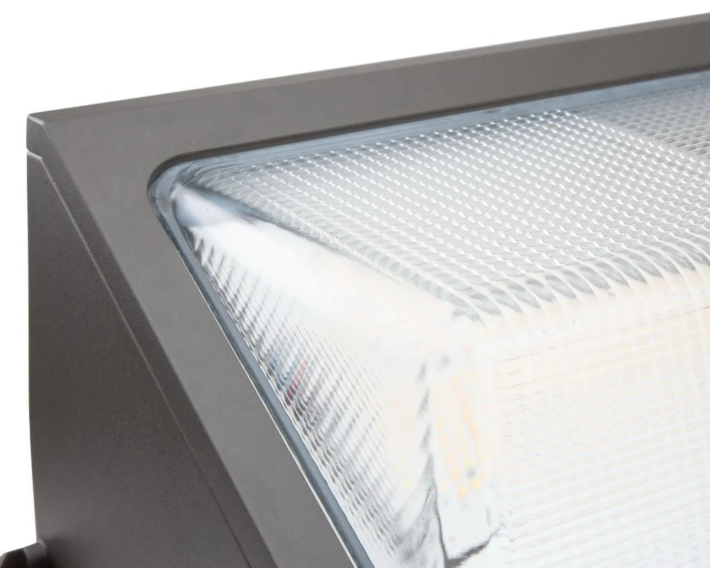 Macro-style lens view of the bronze LED wall pack showing the textured lens and fixture bezel; 30/40/50/60W, 4,770–9,471 lm, 3000K/4000K/5000K, IP65, 0–10V dimming, 120–277V.