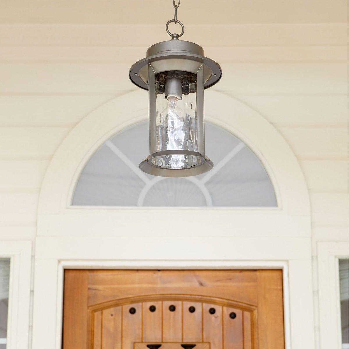Mid Century Modern Outdoor Hanging Light with hammered glass panes, clean-lined drum silhouette, and durable metal construction. Casts a bright light on your outdoor space.