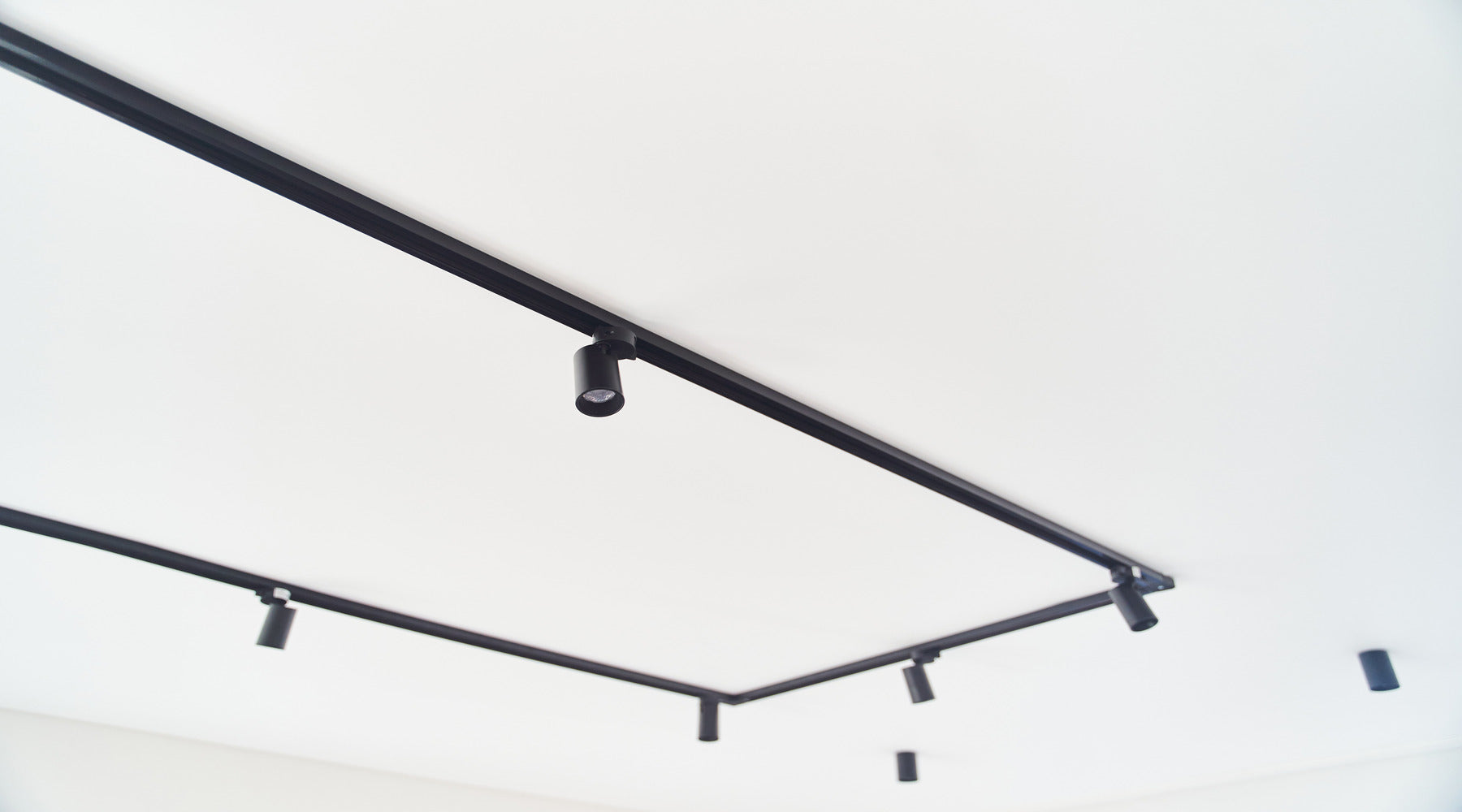 Modern black track lighting installed against white concrete ceiling