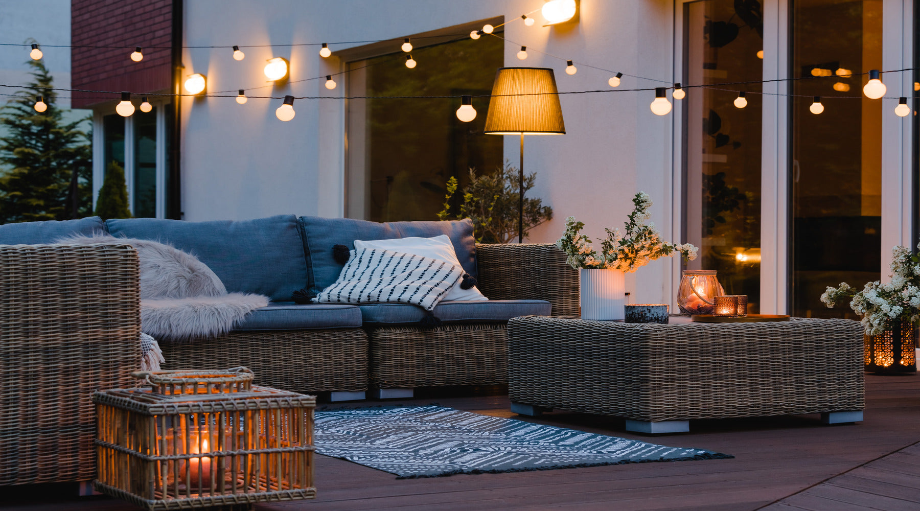 Patio of suburban home with garden being illuminated with outdoor string lights on summer evening